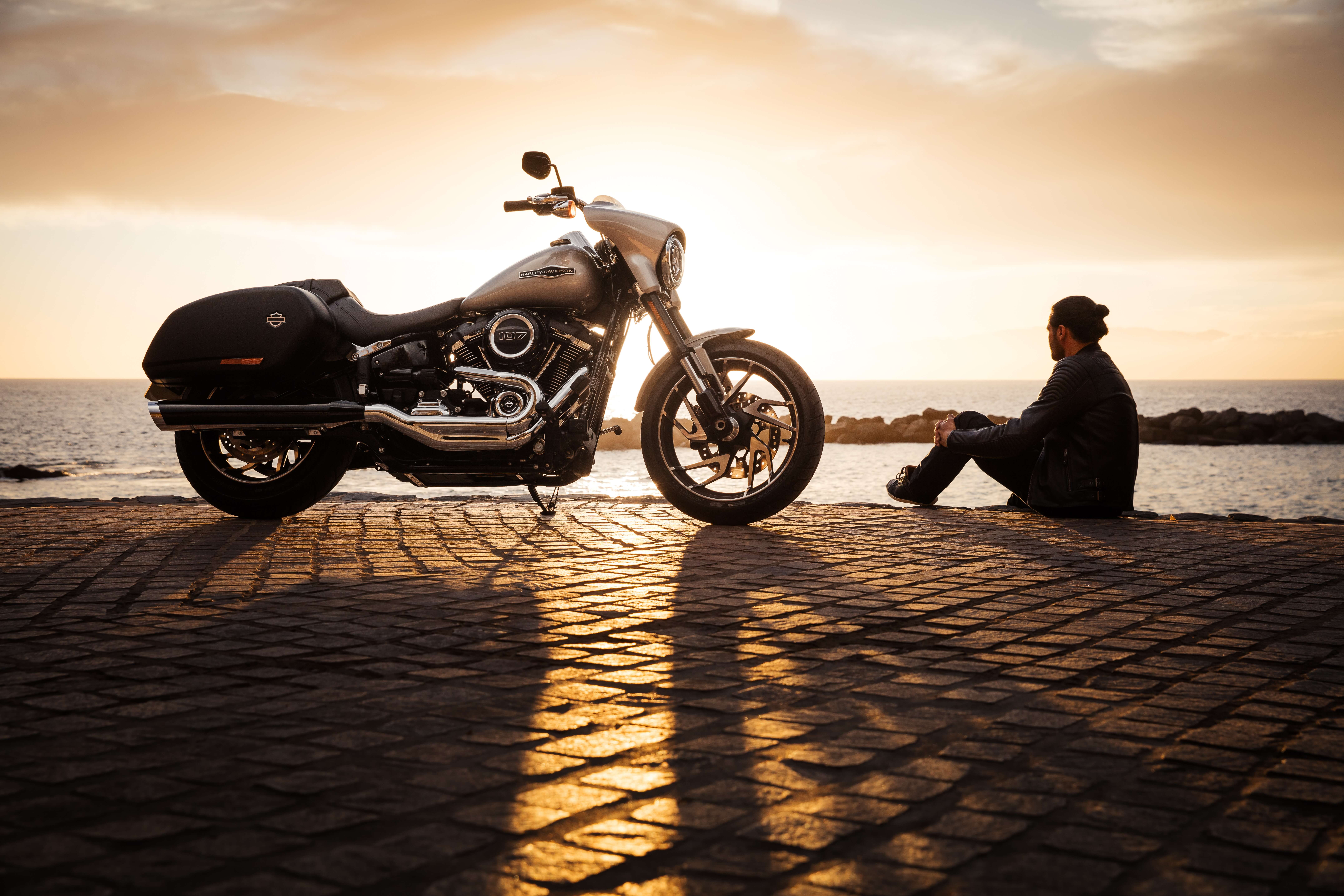 Photo d'un motard et sa moto en silhouette sur le bord de l'eau au coucher du soleil, par harley davidson