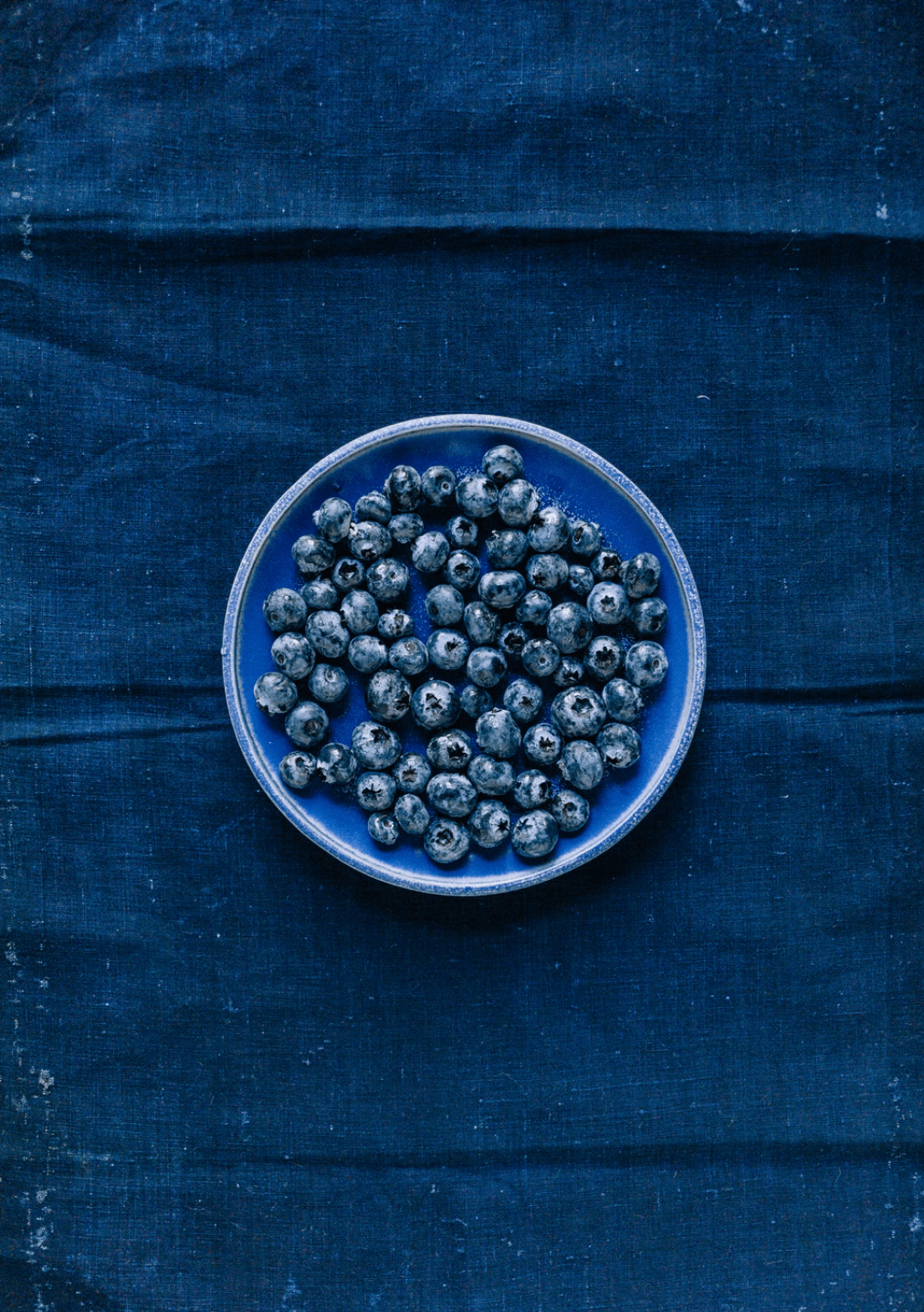 bleuets ou myrtilles dans une assiette bleue déposée sur une nappe bleue